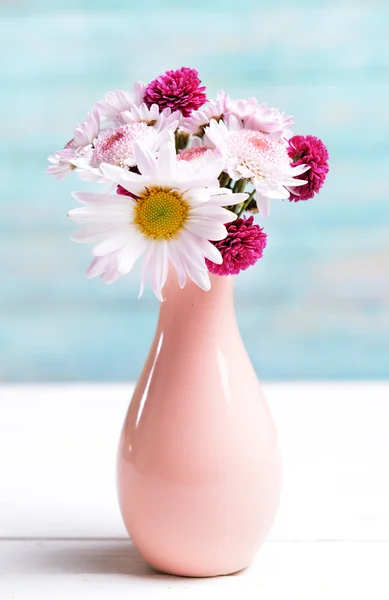 Beautiful flowers in vase on table on light blue background