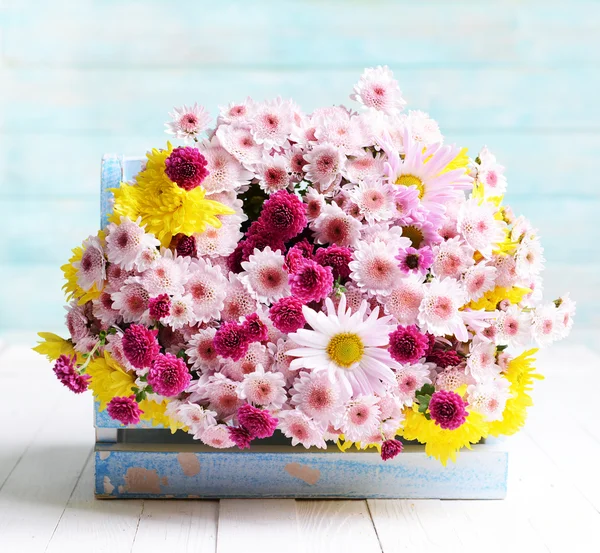 Beautiful flowers in box on table on light blue background