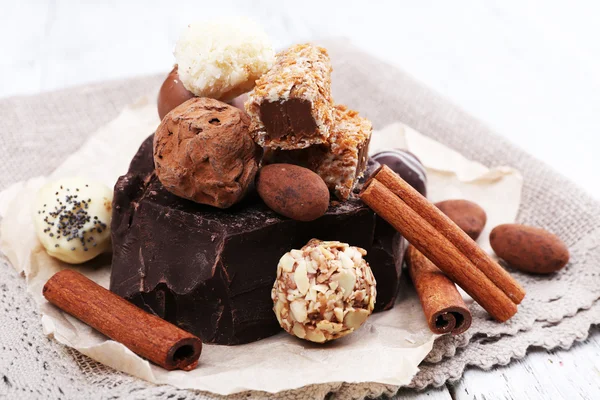 Pile of chunk of chocolate and truffles with cinnamon stick on crumbled paper, grey material and wooden background