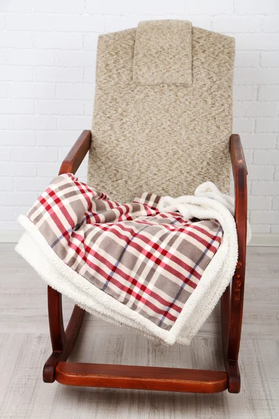 Comfortable rocking-chair with rug on wooden floor near the brick wall background