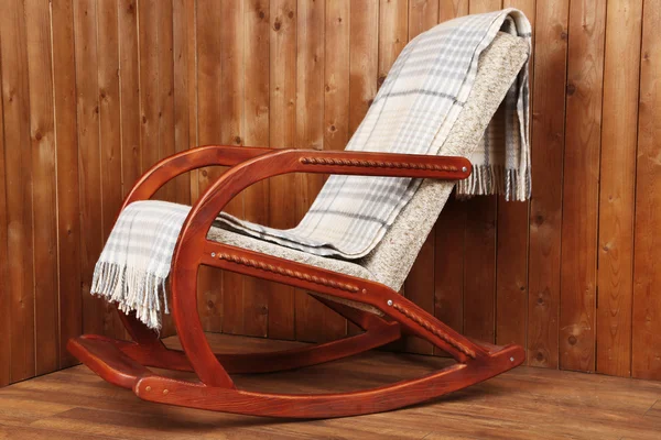 Rocking chair covered with plaid on wooden wall background