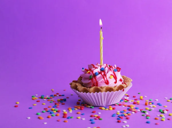 Birthday cup cake with candle and colorful sparkles on purple background