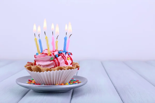 Birthday cup cake with candles on saucer and sparkles on color wooden table and light background