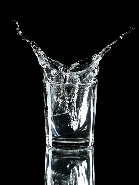 Water splash with ice in glass isolated on black