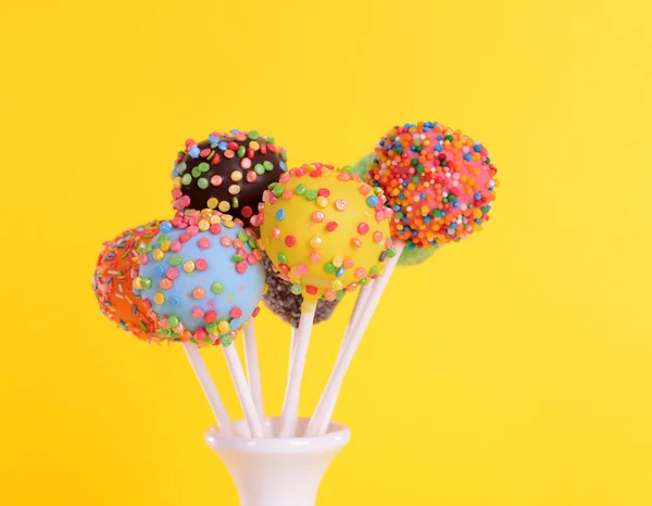 Sweet cake pops in vase on yellow background