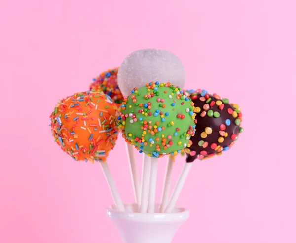 Sweet cake pops in vase on pink background