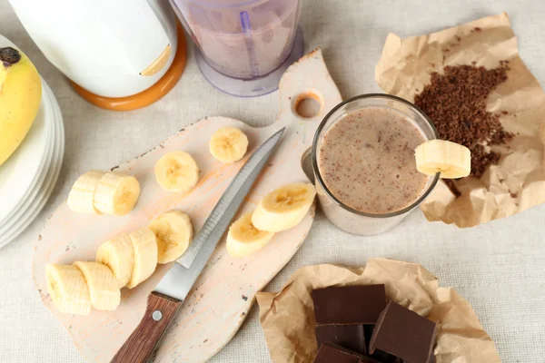 Sliced banana on cutting board and chopped chocolate, on wooden background