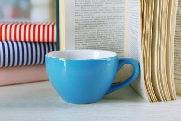 Color cup of tea with books on table, on light blurred background