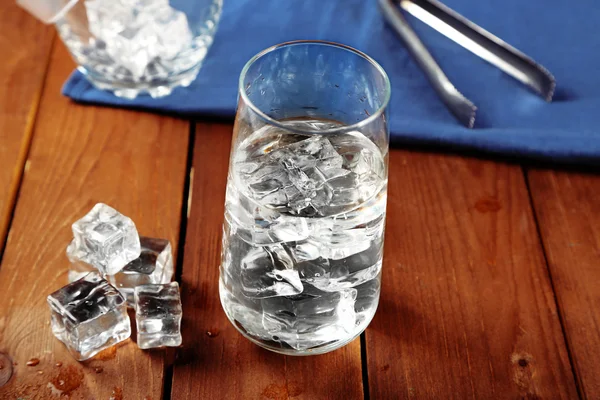 Glass of water with ice on napkin on wooden table background