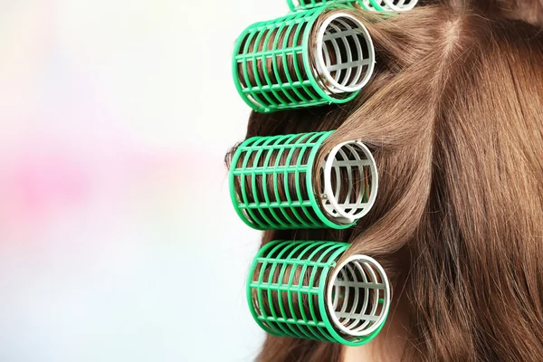 Long female hair during hair dressing with curler, close-up, on light background