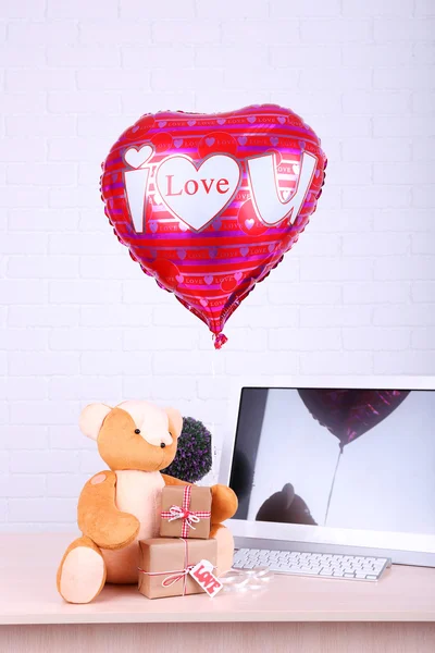 Teddy bear with present boxes, plant and love heart balloon on wooden  computer table, on the brick wall background