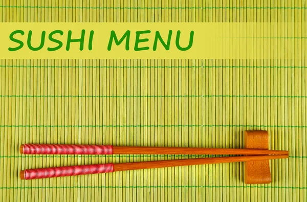 Pair of chopsticks and Sushi Menu text on green bamboo mat background