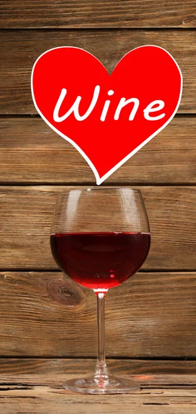 Glass of red wine and sample text in heart on wooden background