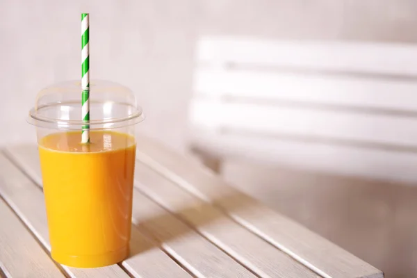 Orange juice in fast food closed cup with tube on wooden table and light wall background