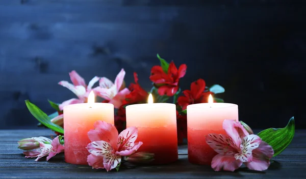 Beautiful candles with flowers on wooden table, on dark background