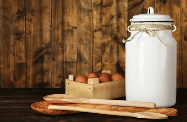 Milk can with eggs and spoons on rustic wooden background