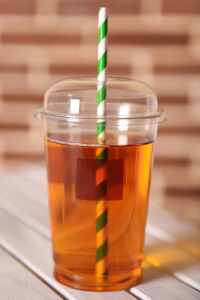 Apple juice in fast food closed cup with tube on wooden table and brick wall background