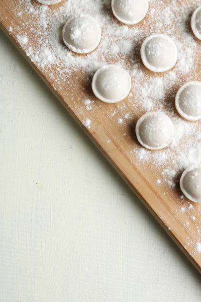 Raw dumplings on cutting board on table close-up