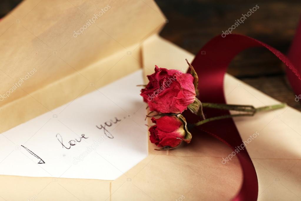 Sobre con carta de amor, cinta vinosa y rosa seca en el fondo de ... Mesa con madera rústica en l