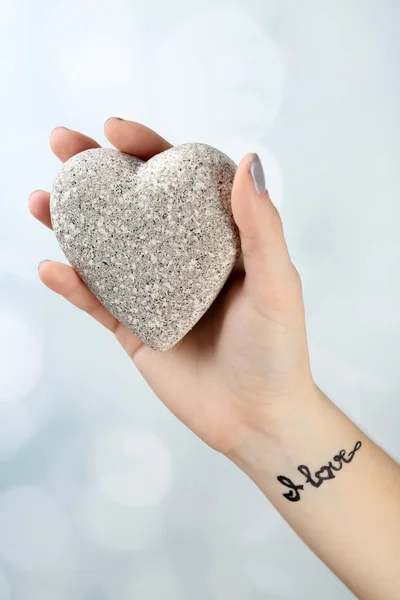 Female arm with tattoo holding decorative heart on light background