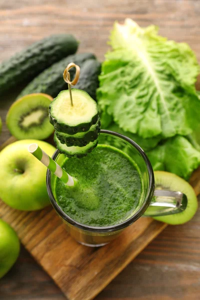 Green fresh healthy juice with fruits and vegetables on cutting board and wooden table background