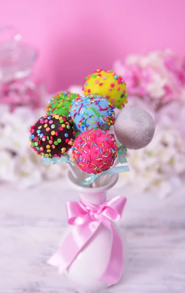 Sweet cake pops in vase on table on pink background