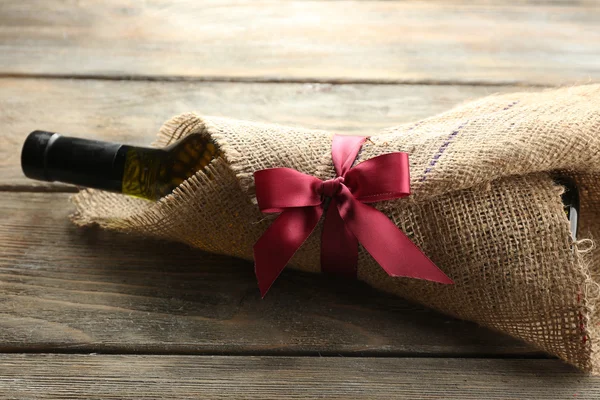 Wine bottle wrapped in burlap cloth on wooden planks background