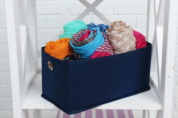 Different scarves in textile box on shelf and white brick wall background