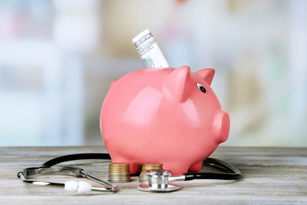 Pink piggy bank with stethoscope on light background
