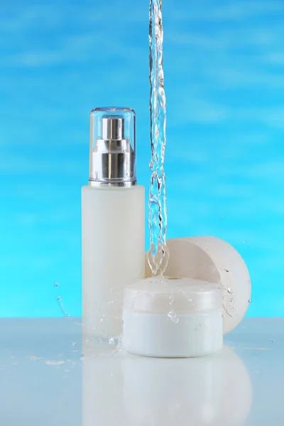 Cosmetic products in water splashes on blue background