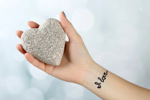 Female arm with tattoo holding decorative heart on light background