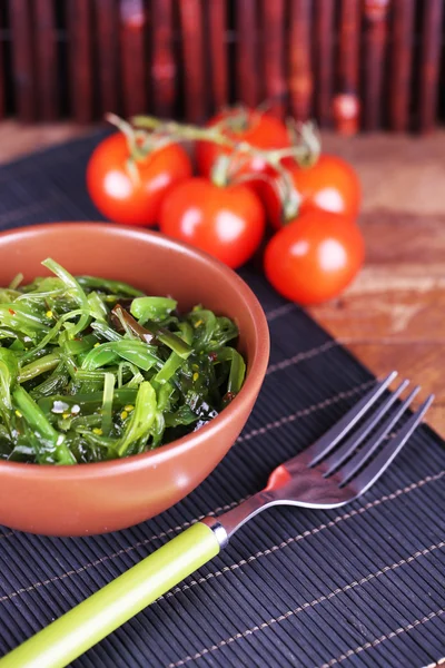 Seaweed salad in bowl with cherry tomatoes on bamboo mat background