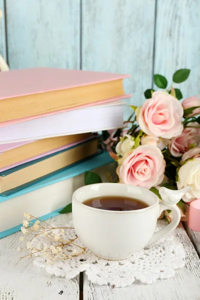 Cup of tea with books and flowers on wooden background