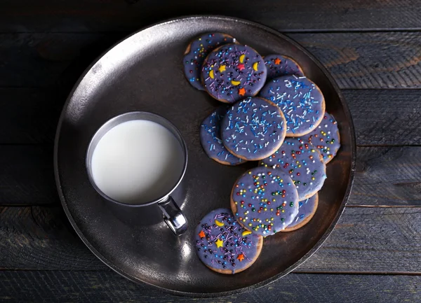 Glazed cookies on metal tray with mug of milk on rustic wooden planks background