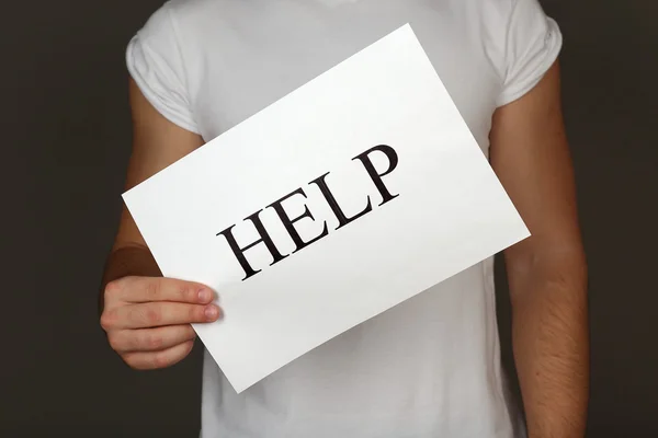 Sheet of paper with Help sign in male hand on dark background