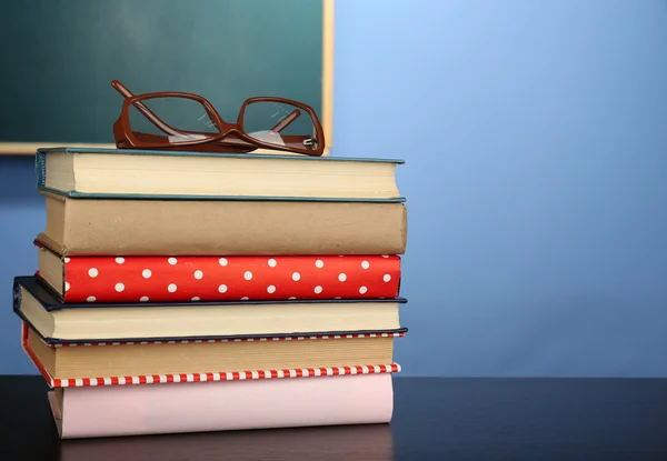 Stack of books with glasses on wooden desk, on colorful wall and blackboard background