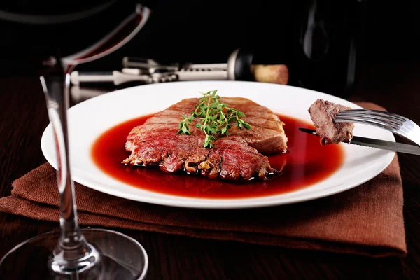 Glass of wine with grilled steak in wine sauce on dark background