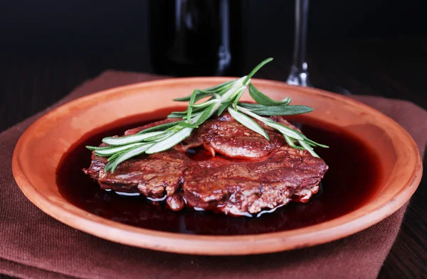 Grilled steak in wine sauce with bottle of wine on dark background