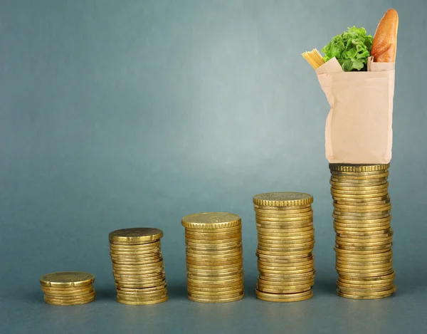 Paper bag with food standing on stack of coins on gray background