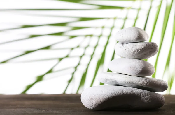 Still life of spa stones on wooden surface with palm leaf isolated on white