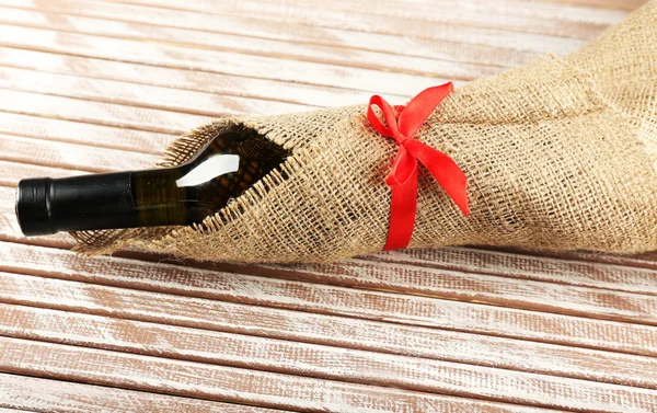 Wine bottle wrapped in burlap cloth on wooden planks background