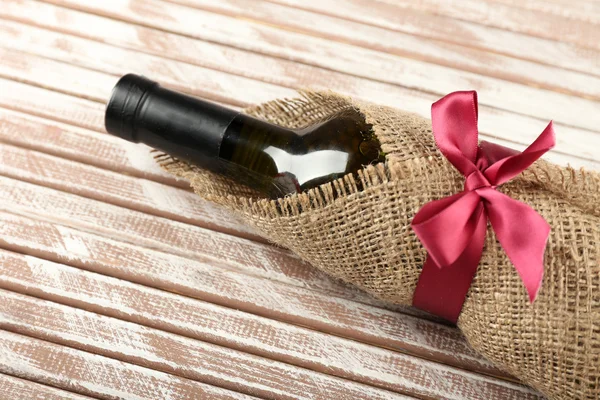 Wine bottle wrapped in burlap cloth on wooden planks background