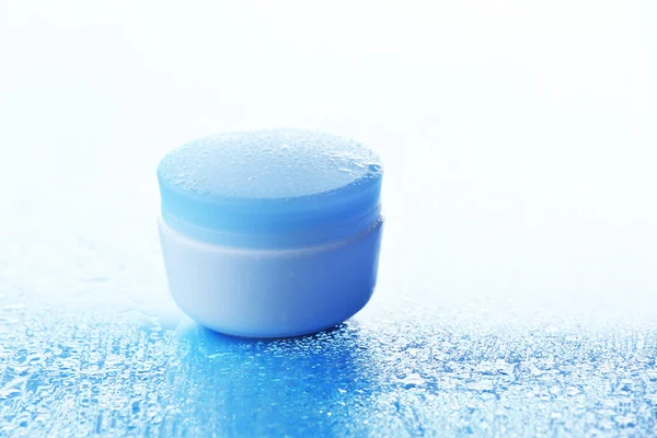Cosmetic cream on blue background with water drops