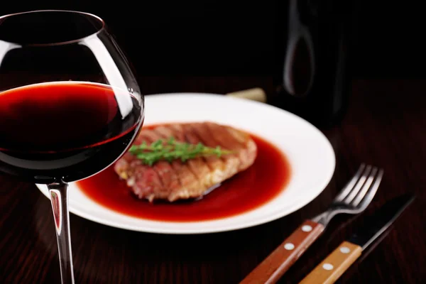 Glass of wine with grilled steak in wine sauce on dark background