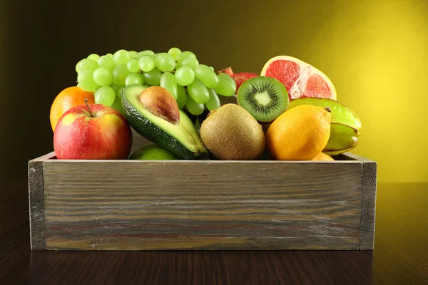 Assortment of fruits in box on dark yellow background