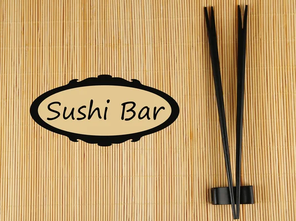 Pair of chopsticks and Sushi Bar text on bamboo mat background