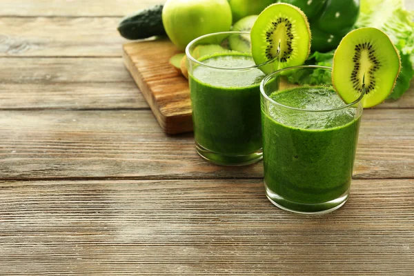 Green fresh healthy juice with fruits and vegetables on cutting board and wooden table background