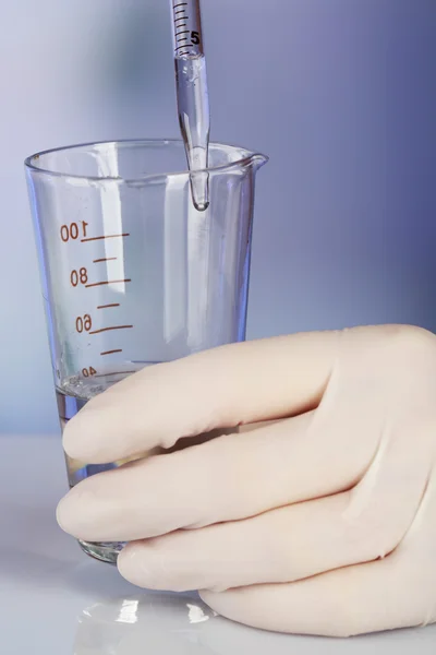 Hand of assistant with liquid in glassware during experiment in laboratory on light blurred background