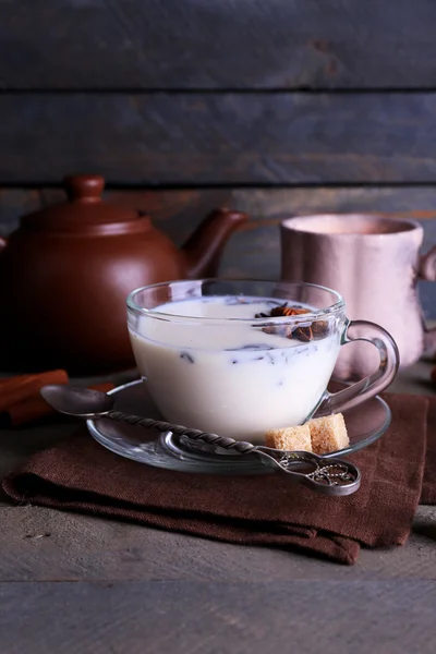 Black tea with milk in cups and teapot with lump sugar on color wooden planks background