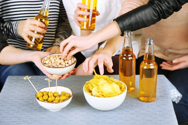 Friends hands with bottles of beer and snacks, close up